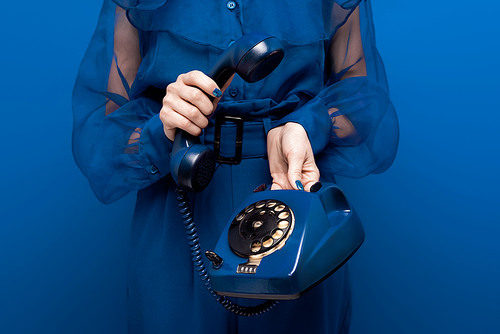 cropped view of woman holding retro telephone on blue background
