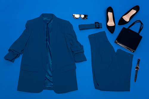 top view of jacket, trousers, heels, belt, bag, wristwatch and sunglasses isolated on blue