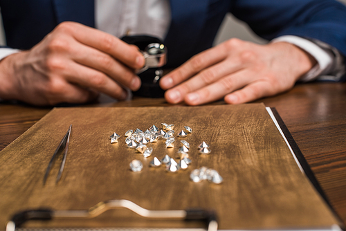 Selective focus of gemstones on board and jewelry appraiser working at table isolated on grey