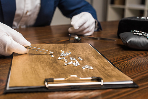 Cropped view of jewelry appraiser with pliers examining gemstones on wooden board on table in workshop