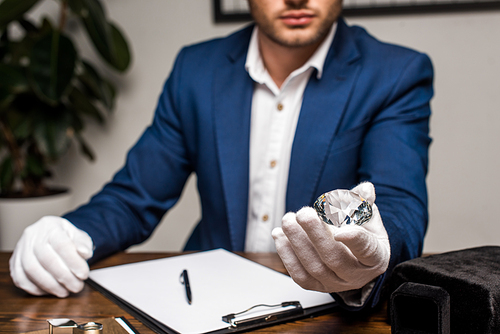 Selective focus of jewelry appraiser holding gemstone near clipboard on table