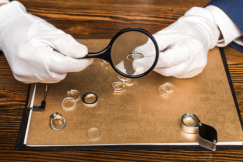 Cropped view of jewelry appraiser holding jewelry ring and magnifying glass near board on table
