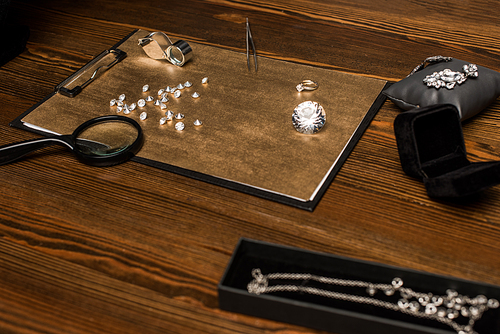 Selective focus of gemstones, jewelry and magnifying glasses with tweezers on board on wooden table