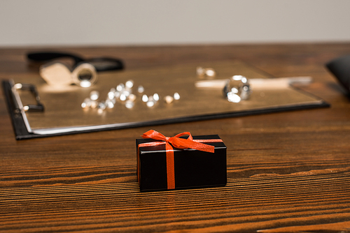 Selective focus of gift box near gemstones on board on table isolated on grey