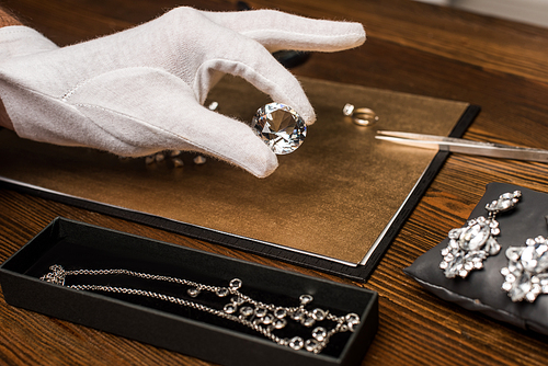 Cropped view of jewelry appraiser holding gemstone near jewelry on board on table isolated on grey