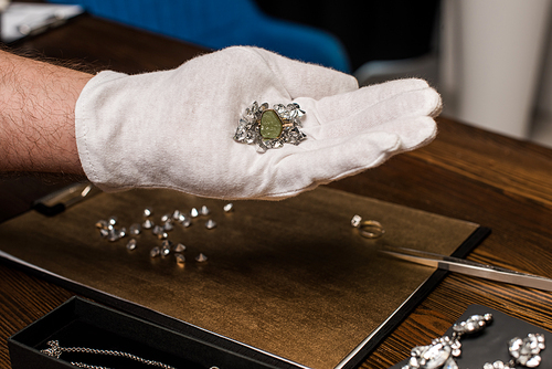 Cropped view of jewelry appraiser holding ring and gemstones near jewelry and board on table