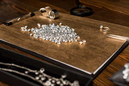 Selective focus of gemstones, magnifying glasses and jewelry on board on wooden table