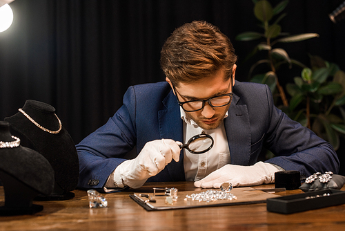 Handsome jewelry appraiser examining gemstones on board with magnifying glass on table