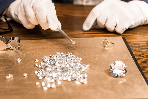 Cropped view of jewelry appraiser holding gemstone in tweezers near board on table