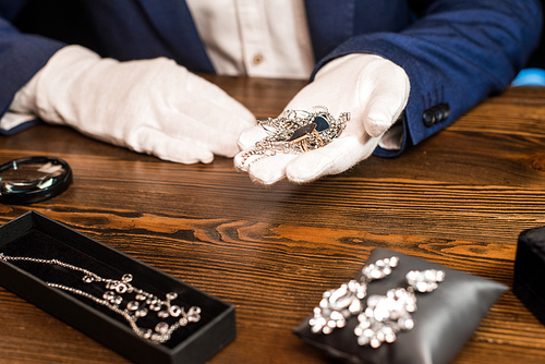Cropped view of jewelry appraiser holding jewelry near magnifying glass on table on black background