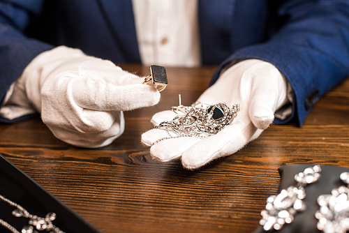 Cropped view of jewelry appraiser holding ring and jewelry at table isolated on black