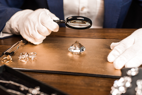 Cropped view of jewelry appraiser examining gemstone with magnifying glass near jewelry on board on table isolated on black