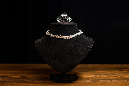 Necklace stand with necklace and diamond on wooden table isolated on black