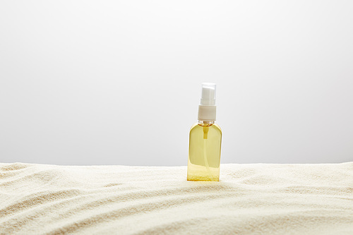 suntan oil in transparent yellow spray bottle in sand on grey background
