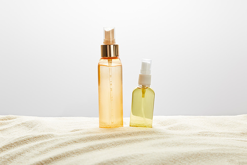 sunscreen products in transparent bottles in sand on grey background