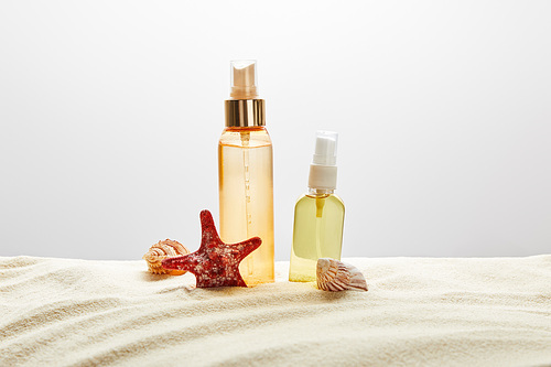 products for suntan in transparent bottles in sand with seashells and starfish on grey background