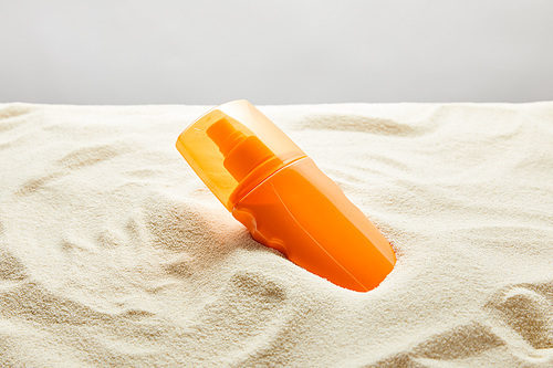 sunscreen in orange bottle in sand on grey background
