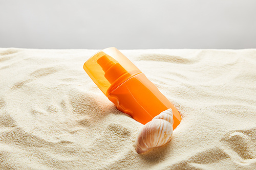 sunscreen in orange bottle in sand with seashell on grey background