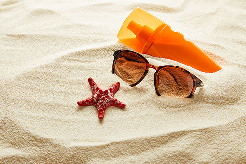 brown stylish sunglasses on sand with red starfish and sunscreen in orange bottle
