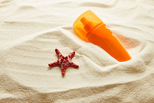 red starfish and sunscreen in orange bottle in textured sand