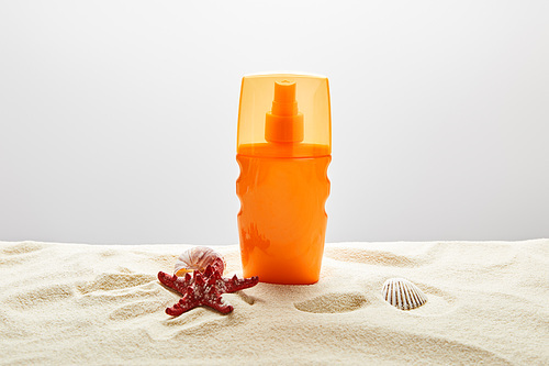 sunscreen in orange bottle with red starfish and seashells on sand on grey background