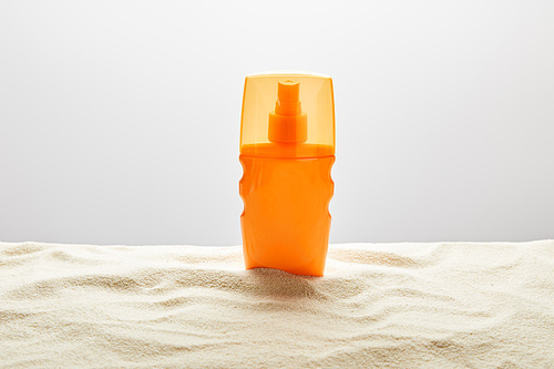 sunscreen in orange bottle on textured sand on grey background