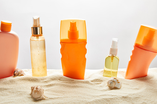 various sunscreen products in bottles on sand with seashells on grey background