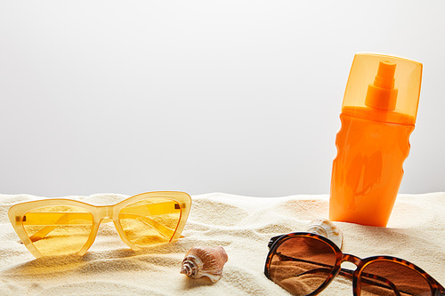 yellow and brown sunglasses and sunscreen in orange bottle on sand on grey background