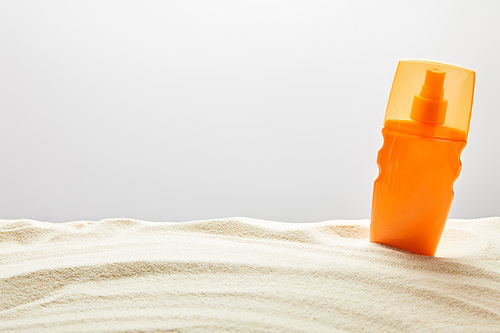 sunscreen cream in orange spray bottle in sand on grey background