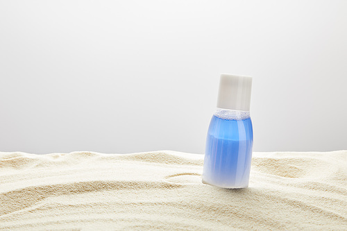 sunscreen blue lotion in bottle in sand on grey background with copy space