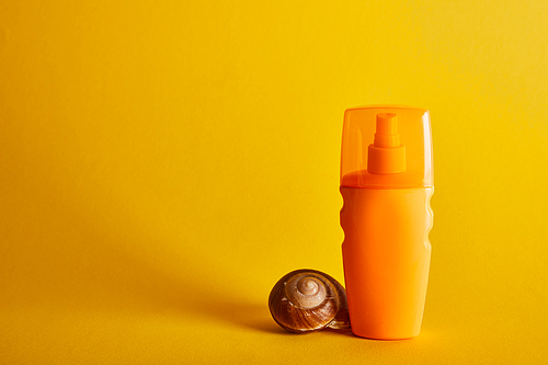 sunscreen in orange bottle near seashell on dark yellow background