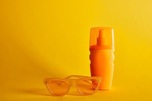 sunscreen in orange bottle near sunglasses on dark yellow background