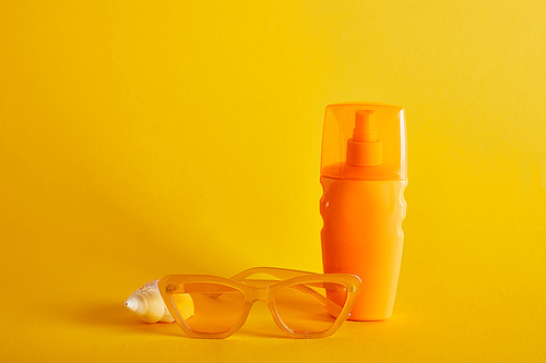 sunscreen in orange bottle near sunglasses and seashell on dark yellow background
