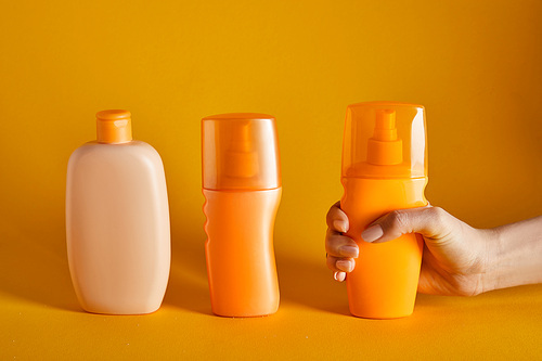 cropped view of woman holding sunscreen near cosmetics in bottles on orange background