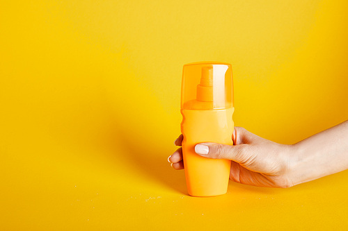 cropped view of woman holding sunscreen in bottle on yellow background