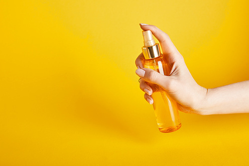 cropped view of woman holding suntan oil in spray bottle on yellow background