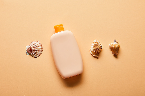 flat lay with sunscreen lotion in bottle and seashells on beige background