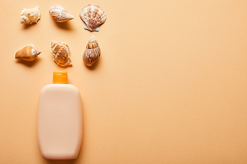 flat lay with sunscreen lotion in bottle near seashells on beige background