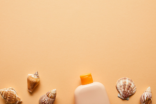 top view of sunscreen lotion in bottle near seashells on beige background