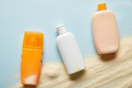 top view of sunscreen products in bottles on blue background with sand