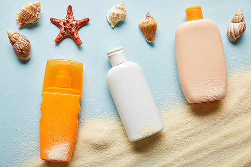 top view of sunscreen products in bottles on blue background with sand, starfish and seashells