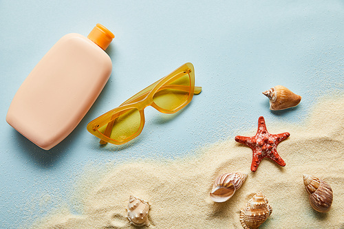 top view of sunscreen in bottle near seashells, starfish, sand and sunglasses on blue background