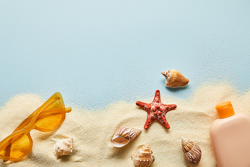 top view of sunscreen lotion in bottle near sunglasses on blue background with sand and seashells