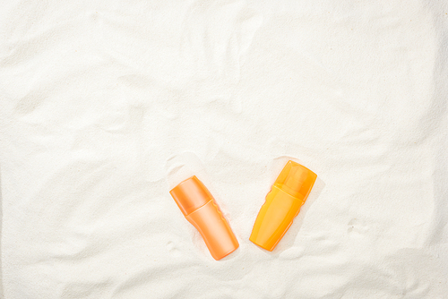 orange bottles of sunscreen on sand with copy space