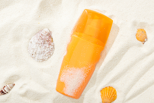 orange bottle of sunscreen on sand with seashells