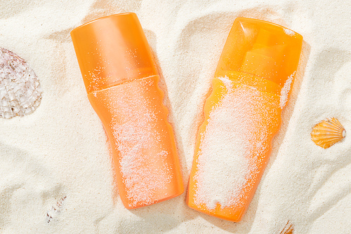 orange bottles of sunscreen on sand with seashells