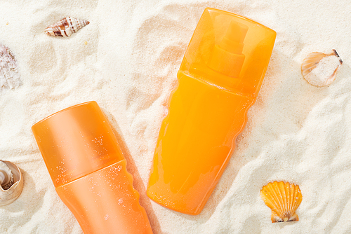 orange bottles of sunscreen on golden sand with seashells