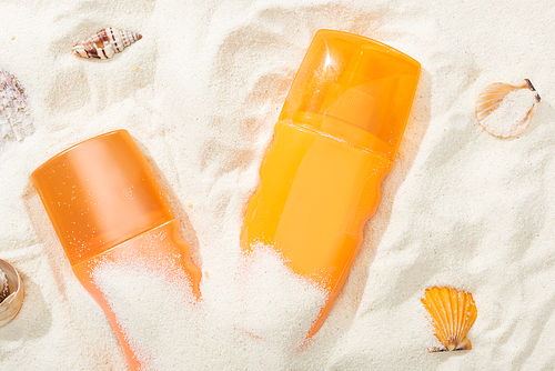 orange bottles of sunscreen lotion on sand with seashells