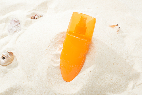 orange bottle of sunscreen in sand with seashells