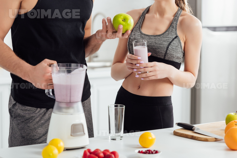 유토이미지 Cropped View Of Man Holding Apple And Blender Near Sportive Girl With Glass Of Smoothie 6596